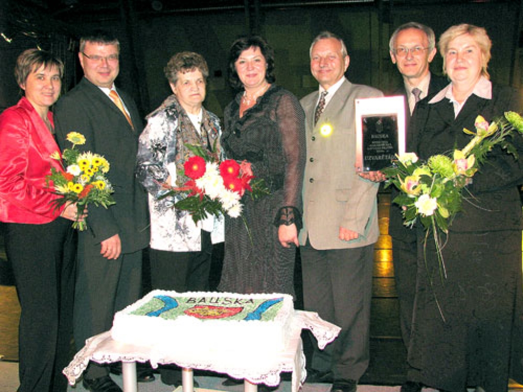 Bauskas Domes darbinieki Sarmīte Oļehnoviča (no kreisās), Māris Freimanis, Ārija Gaile, Jānis Mičulis, Voldemārs Čačs un Daina Nikolajeva kopā ar Latvijas Pilsētu savienības priekšsēdētāju Nelliju Kleinbergu (vidū) priecājas par iegūto balvu un rāda Bauskas pilsētas dāvanu šajā pasākumā – īpaši gatavotu torti ar Bauskas ģerboni.