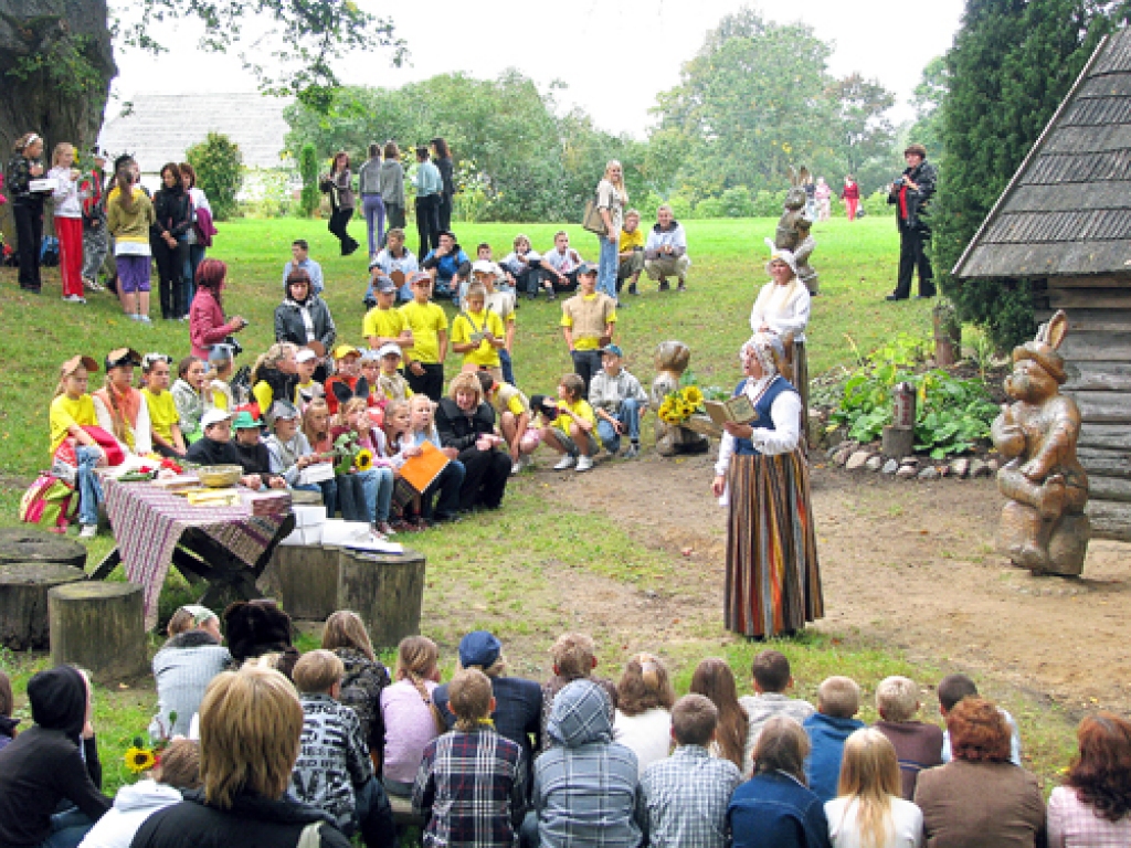 Vija Cerusa (centrā tautastērpā) vada skolēnu pasaku un dzejas pēcpusdienu pie «Zaķīšu pirtiņas» Plūdoņa muzejmājā.