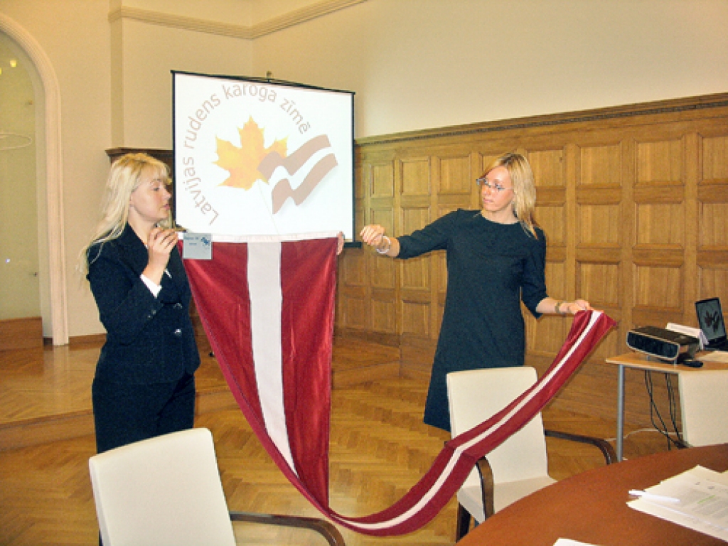Ārlietu ministrijas darbinieces Sintija Stipre (no kreisās) un Zane Ampermane demonstrē jauno Latvijas karoga vimpeli. 