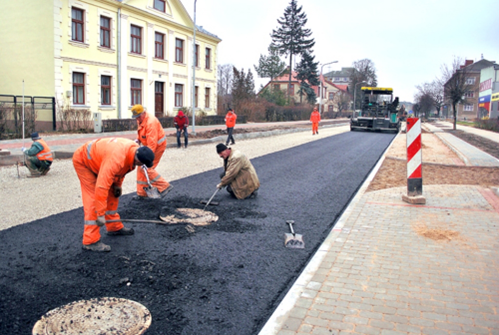 Uzvaras ielā Bauskā sākusies asfalta ieklāšana – strādnieki paceļ kanalizācijas lūkas līdz vajadzīgajam līmenim.