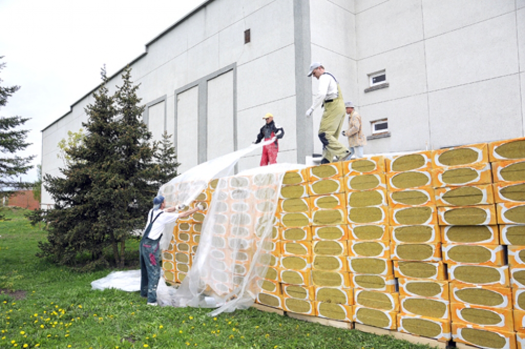 SIA «Riveta» strādnieki apklāj ar plēvēm otro akmensvates plākšņu kravu, kas paredzēta Īslīces kultūras nama siltināšanai.