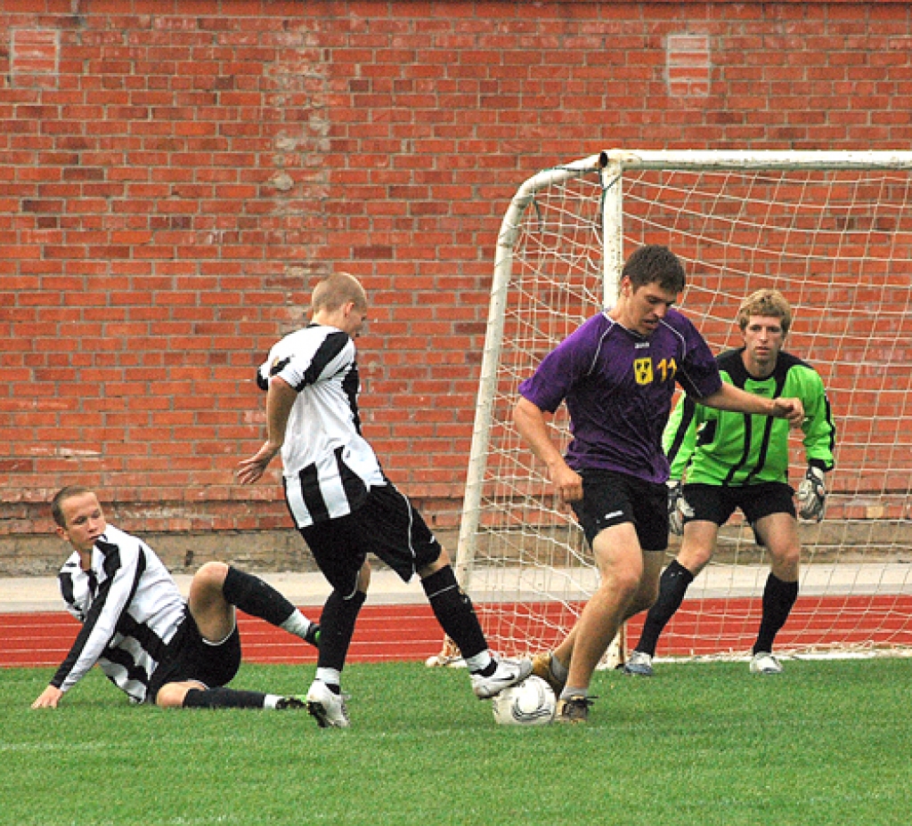 «Īslīces» futbolisti (balti melnajos tērpos) pie saviem vārtiem mēģina apturēt «Gailīšu» uzbrucēju.