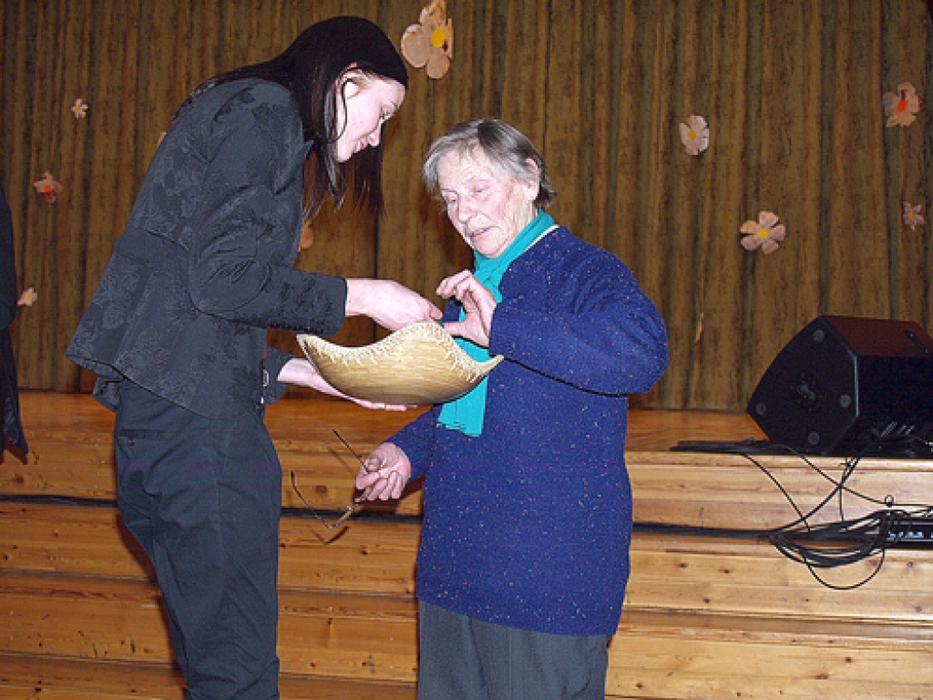 Maija Māla (no kreisās), virtuālās enciklopēdijas pētniece, saņem piemiņas nozīmīti no Rasmas Mažānes, iespējams, daudzkrāsainākā dzīvesstāsta īpašnieces Iecavas novadā.