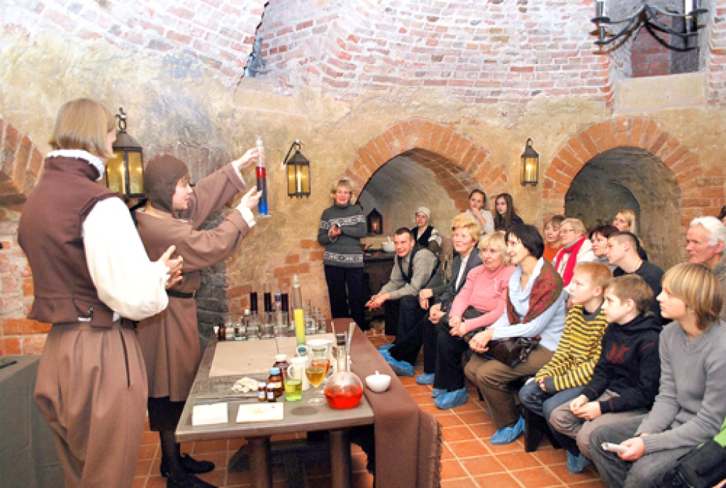 Meistars jeb Mihails Haļitovs klātesošajiem rāda: «Šis ir dzīvības eliksīrs, pārbaudīts. Kad suns iedzer, trīs dienas skraida gaudodams.»