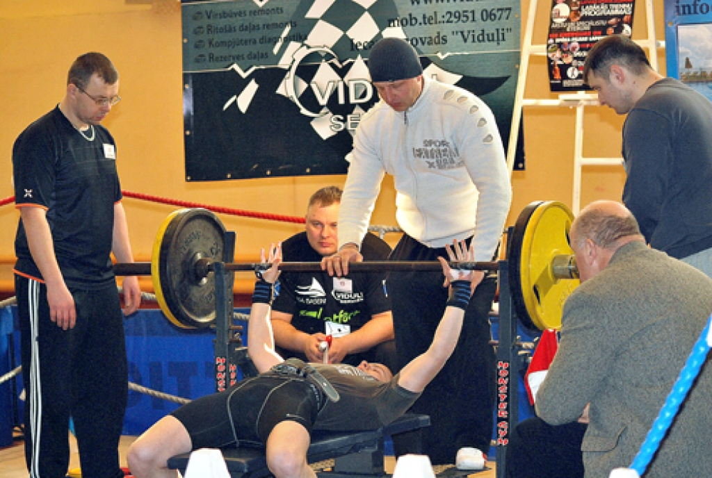 Baušķenieks Juris Ručkanovs uzspieda 110 kilogramu svara stieni. Viņam palīdz Felikss Žieds, jaunā sportista veikumu vēro tiesnesis Andrejs Mūrnieks (sēž vidū).