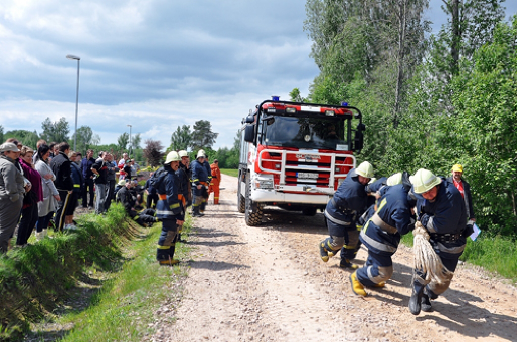 Kolēģi un līdzjutēji vēro, kā smago automobili velk Bauskas ugunsdzēsēju komandas vīri. 
