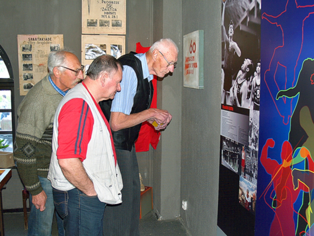 Leģendārais basketbolists Visvaldis Eglītis (no labās) sporta nama «Dartija» direktoram Guntim Pakalnam un veterānu sportistam Ojāram Pārumam nosauc paša sasniegumiem veltītajā stendā redzamos reiz tikpat slavenos komandas biedrus.