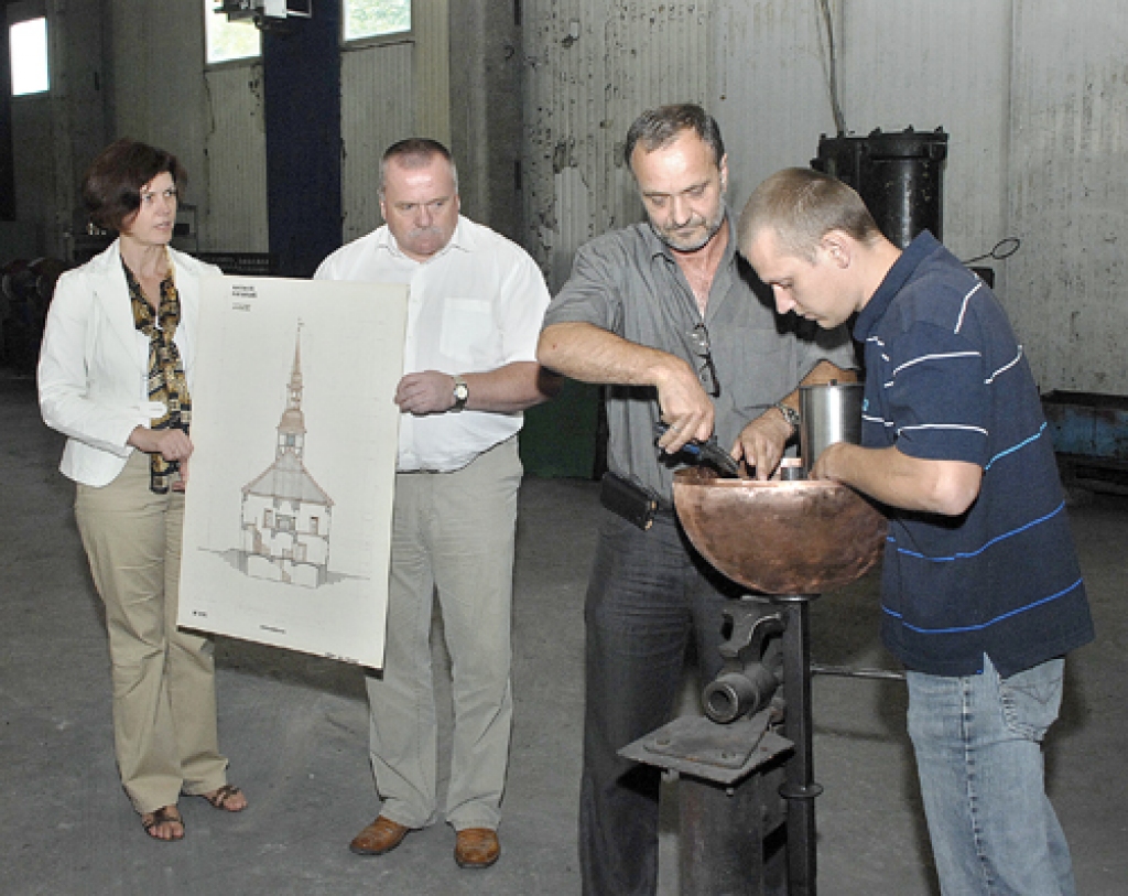 Kapara lodē ievietota kapsula ar vēstījumu. Bauskas kalējmeistari Uldis Šulcs (priekšplānā no kreisās) un Juris Balakāns aizvērs lodi un pie tās piestiprinās vējrādītāju. Attēlā arī Bauskas novada domes priekšsēdētājs Valdis Veips un attīstības un plānošanas nodaļas vadītāja Ilze Tijone.
