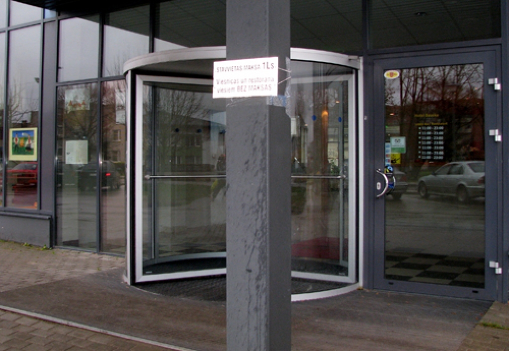 Pie viesnīcas ieejas piestiprinātais uzraksts informē, ka stāvvietas izmantošana ir par maksu. Tas gan attiecas tikai uz laukuma malu tieši pretim viesnīcas ieejai. 
Autors: Vilnis Auzāns