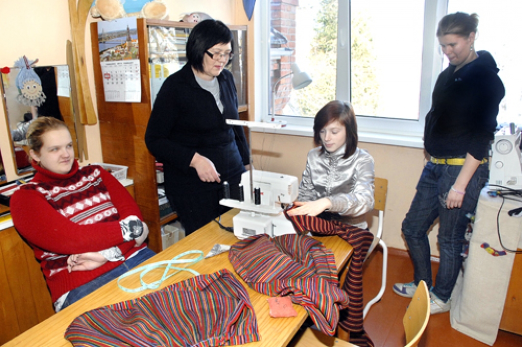 Skolotāja Mārīte Kokoriete meitenēm ierāda, kā apstrādāt svārku vīles ar speciālo šujmašīnu.