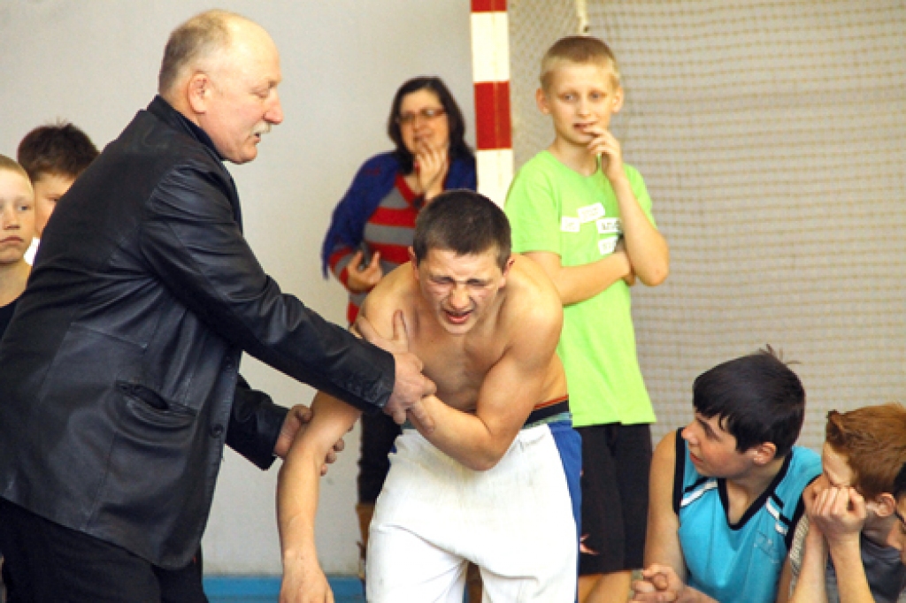 Treneris Vladimirs Iļjins (no kreisās) palīdz traumu guvušajam cīkstonim. 