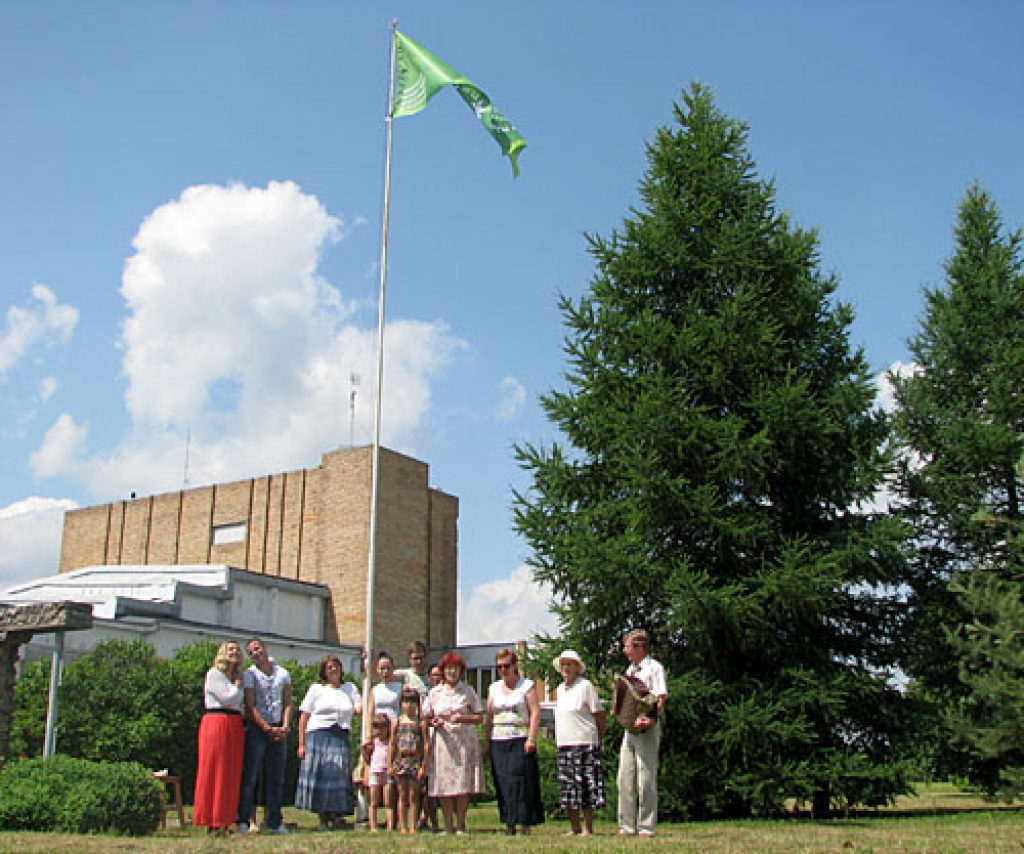 Mastā pie Grenctāles kultūras nama uzvijies zaļš karogs. Tā zīmējumu veido jauktā kora «Grenctāle» dalībnieku iedziedātās dziesmas «Tu esi latvietis» motīvi. 
Autors: Vilnis Auzāns