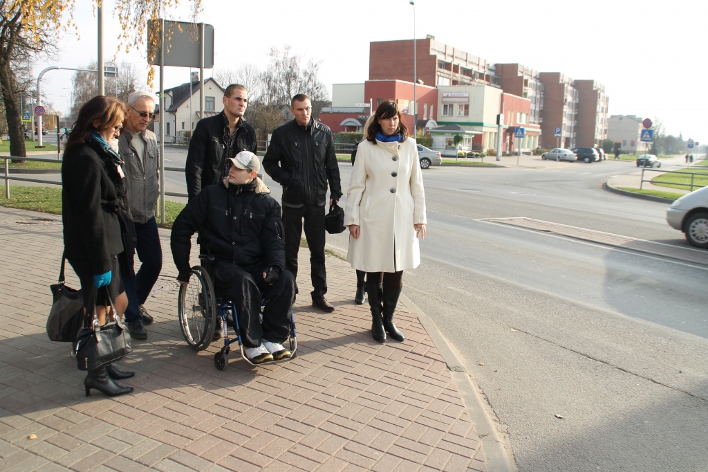 Deniss Juhņevičs (ratiņkrēslā) stāsta par nepatīkami viltīgo ietves nobrauktuvi uz Zaļo ielu. 
Autors: Uldis Varnevičs