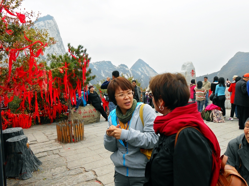 Gide Linda, īstajā vārdā Vanga Da Džīna, kopā ar raksta autori visaugstākajā no daoistu pieciem svētajiem kalniem – Huašan, 2610 m. Pat šajā virsotnē dominē sarkanā krāsa. Lentītes te nes un sien gan svētceļnieki, gan mīlētāji. Līdzīgi kā Latvijā, jaunlaulātie dažādās vietās pieķēdē atslēgas.
Autors: Solveiga Ikerte