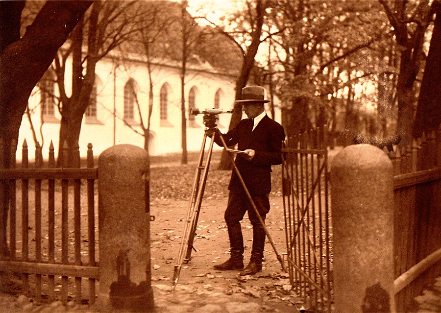 Skats uz baznīcas dārzu 1930. gados no Pils (tagad – Plūdoņa) un Lielās Baznīcas (tagad – Baznīcas) ielas krustojuma. Labi saskatāmi vārtiņi un žoga elementi, aiz vārtiņiem darbojas mērnieks ar teodolītu.
Autors: no Bauskas muzeja krājuma.