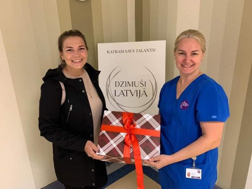 Baušķeniece Liene Breijere ar pērn aizvesto dāvinājumu – zeķītēm kārbā, ko vēl šogad saņem Dzemdību namā īpašajos datumos pasaulē nākušie mazuļi. No labās – vecmāte Baiba Zelka.
Autors: no personiskā arhīva.